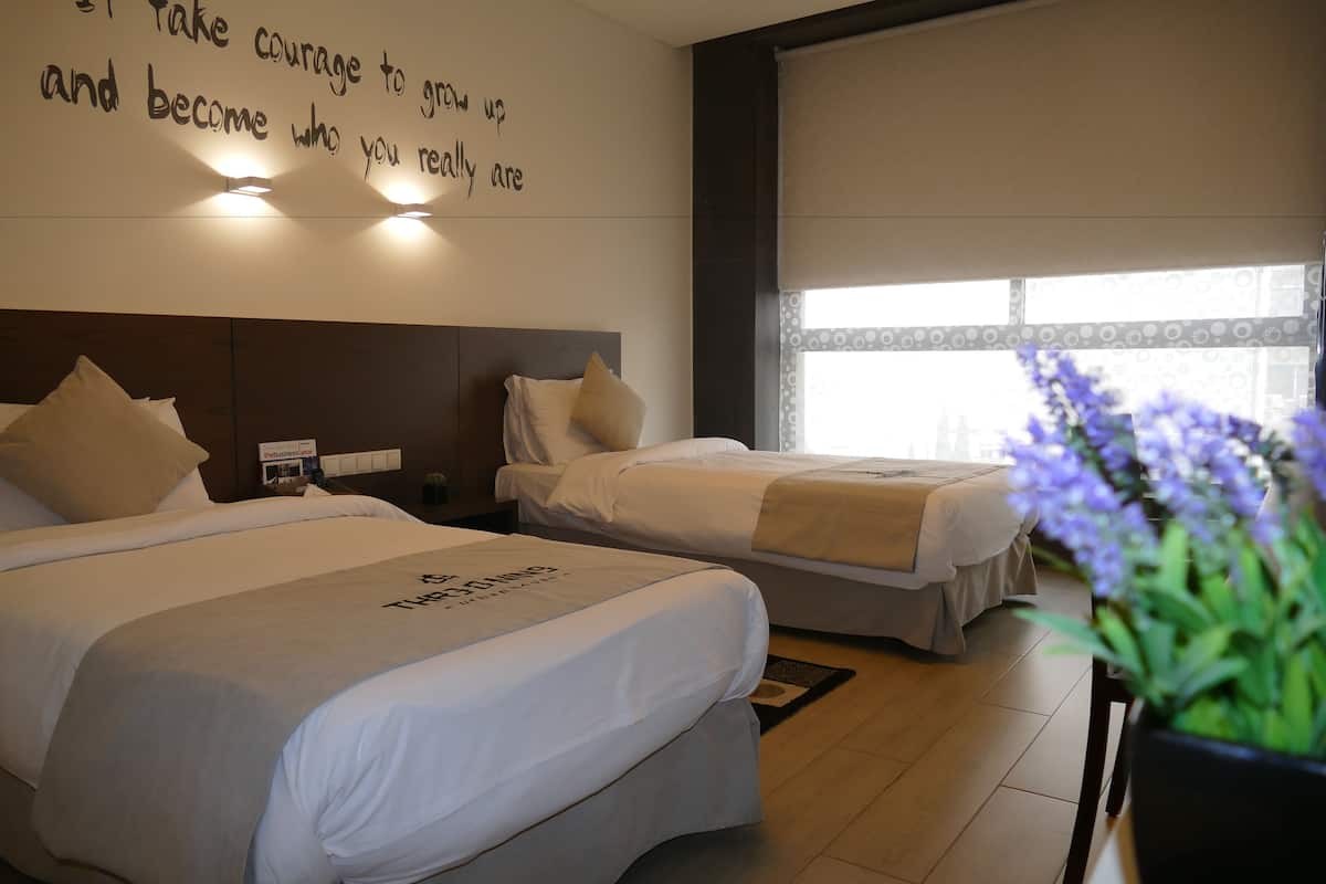 Habitación de hotel con dos camas, una cita motivacional en la pared y un ventanal con persianas.