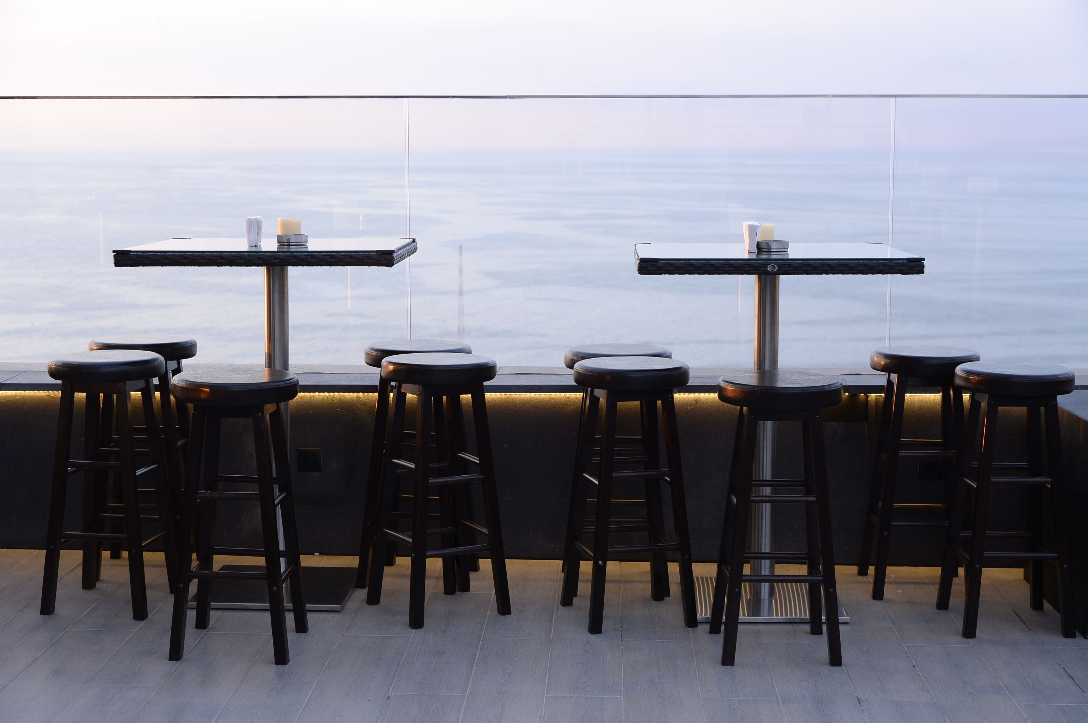 A rooftop bar with tables and stools, overlooking a cityscape.