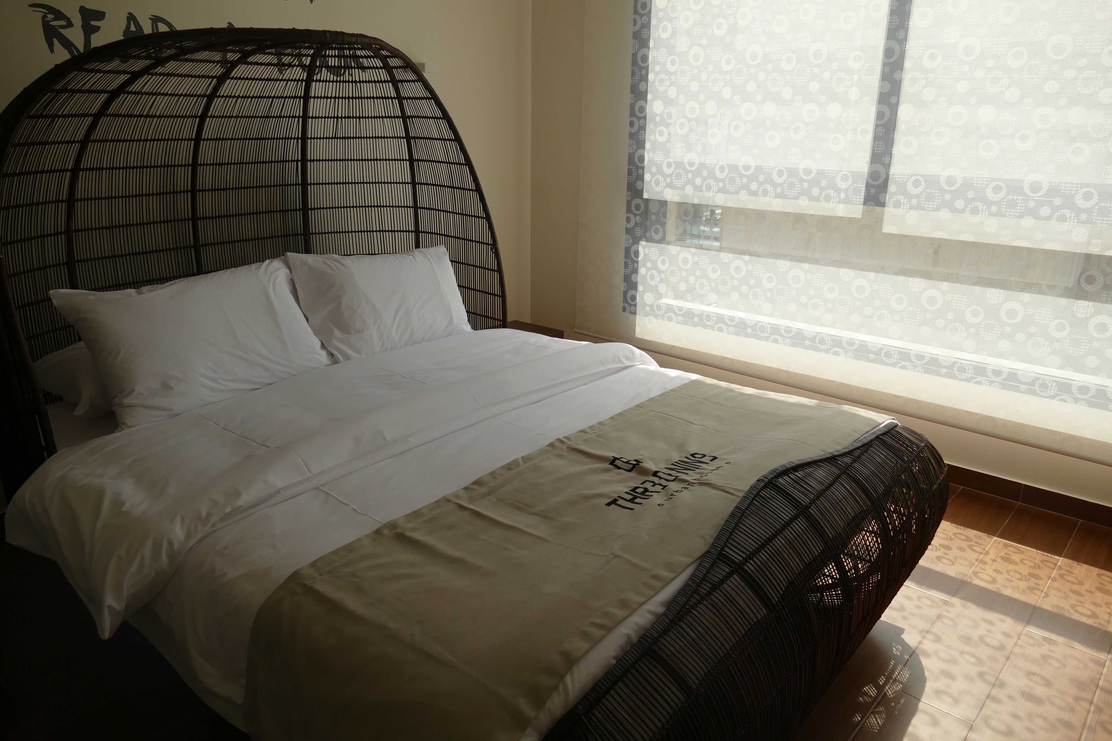 A bed with a headboard, a window with patterned curtains, and a wall with a partial text.