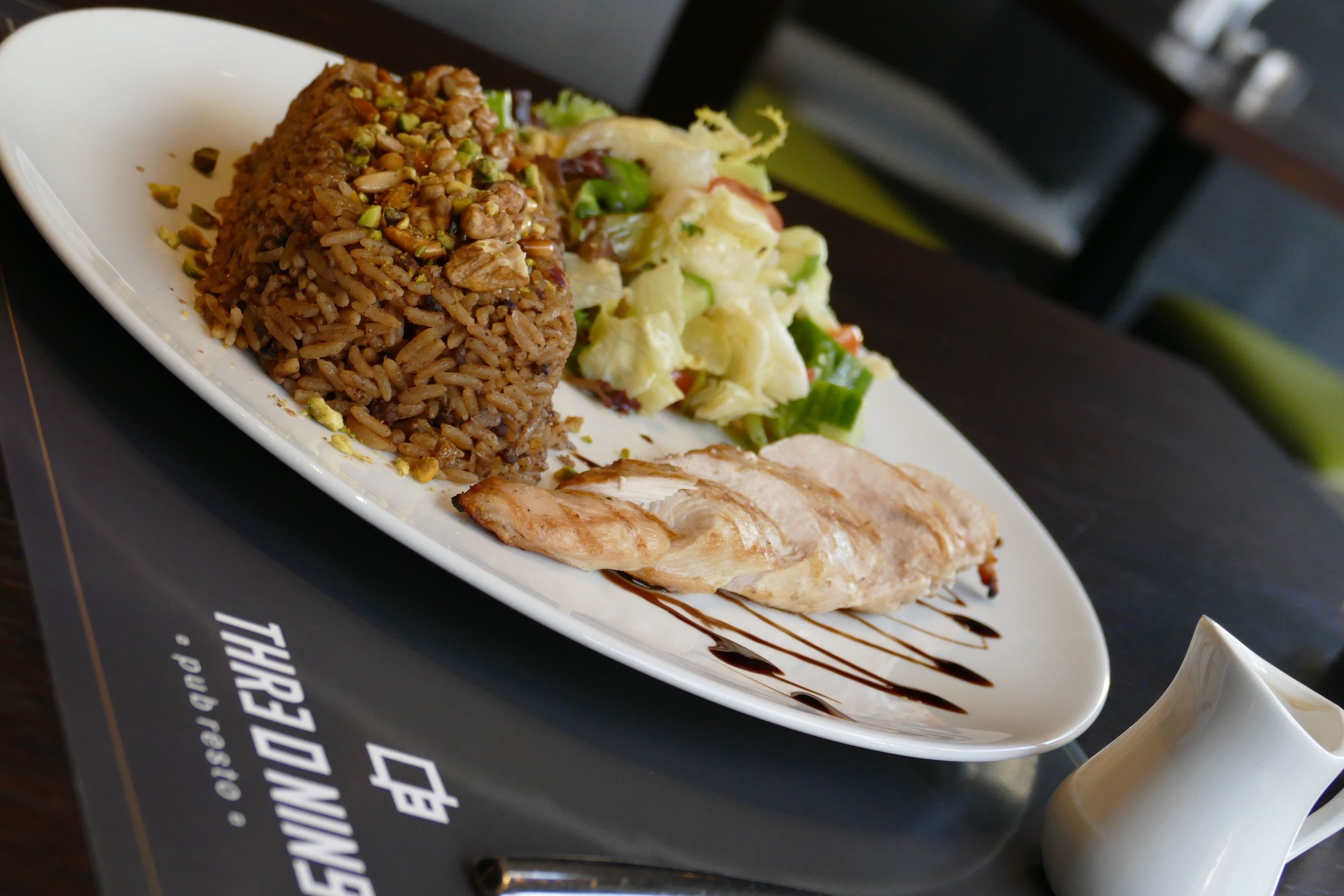 Un plato de comida con arroz, verduras y un trozo de pollo sobre un plato blanco.