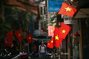 A narrow street with multiple Vietnamese flags, a sign for 'Hotel Bluebird', and a shop named 'COMPLET - VESTUN'. - Bluebell Hotel (Hanoi)