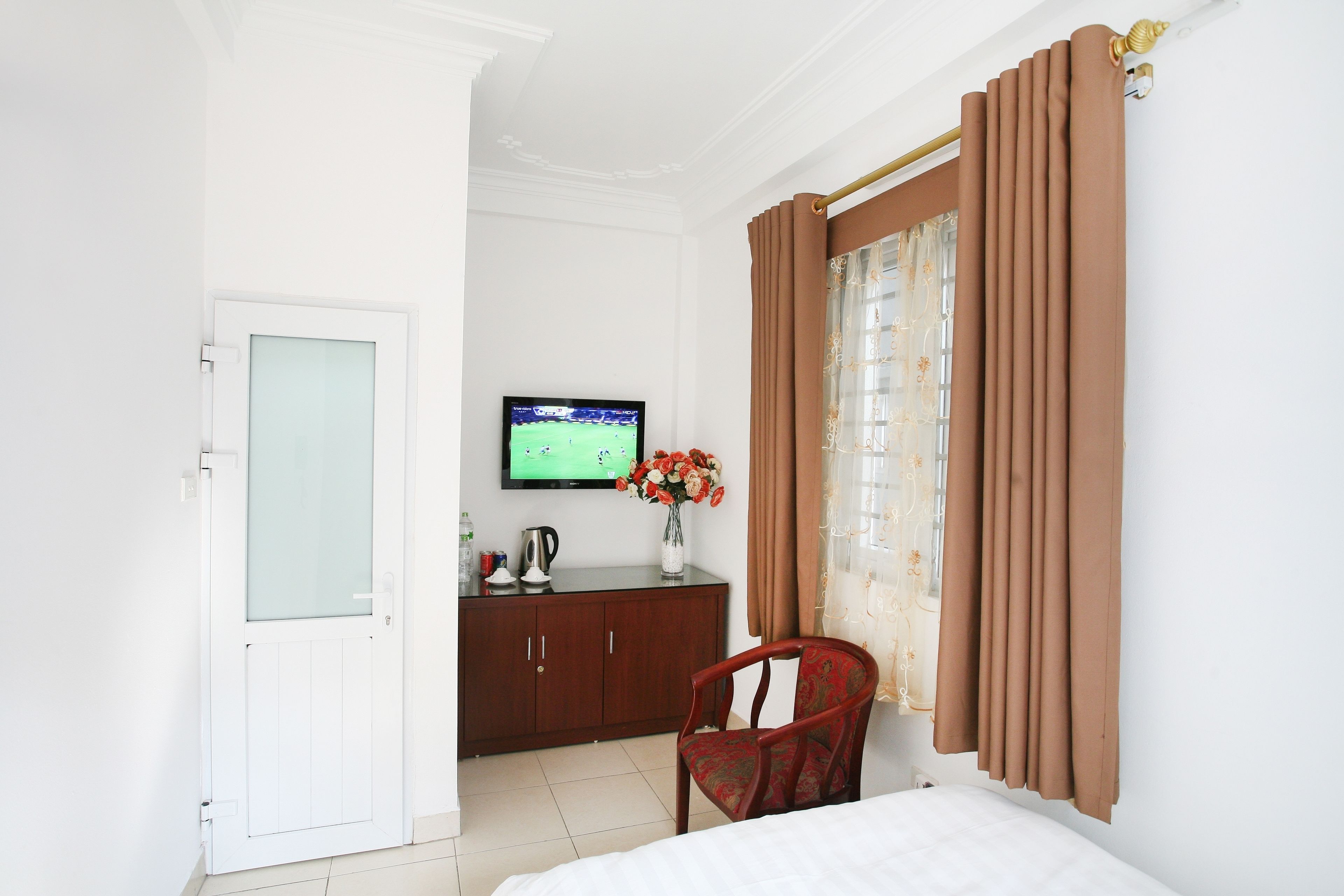 Habitación de hotel con cama, cómoda de madera, televisor y un jarrón con flores.