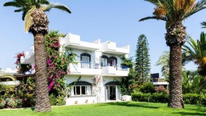 A two-story building with balconies, surrounded by palm trees and greenery. - Gorgona Hotel (Malevizi)