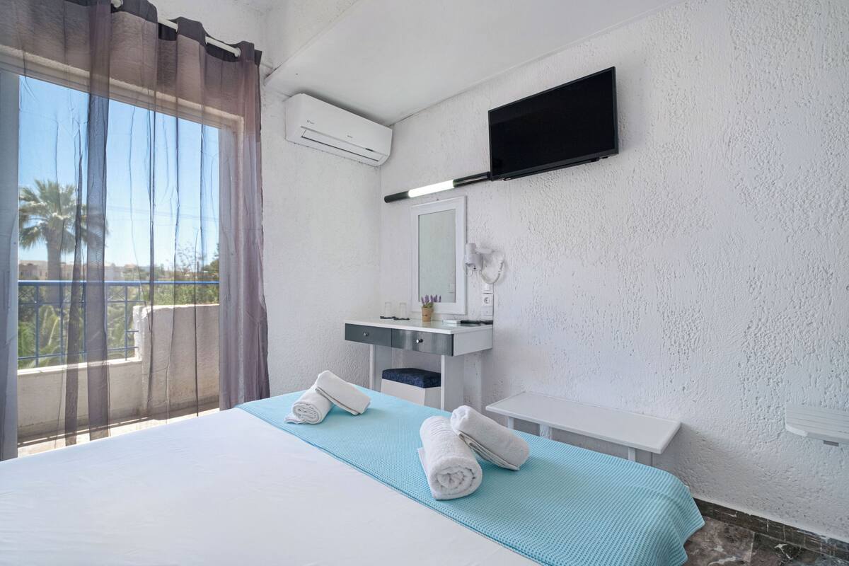 A hotel room with a bed, a bathroom with a mirror, a TV, and a window with curtains.