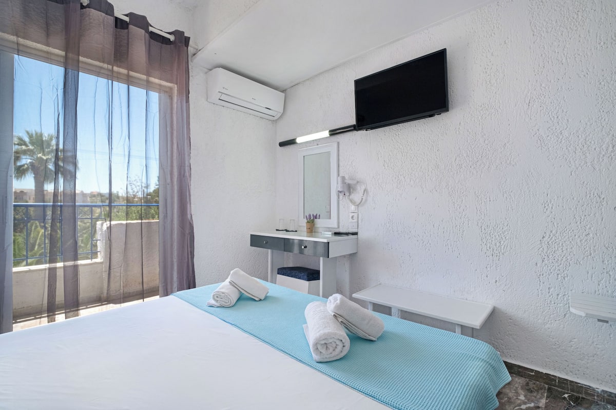 A hotel room with a bed, a bathroom with a mirror, a TV, and a window with curtains.