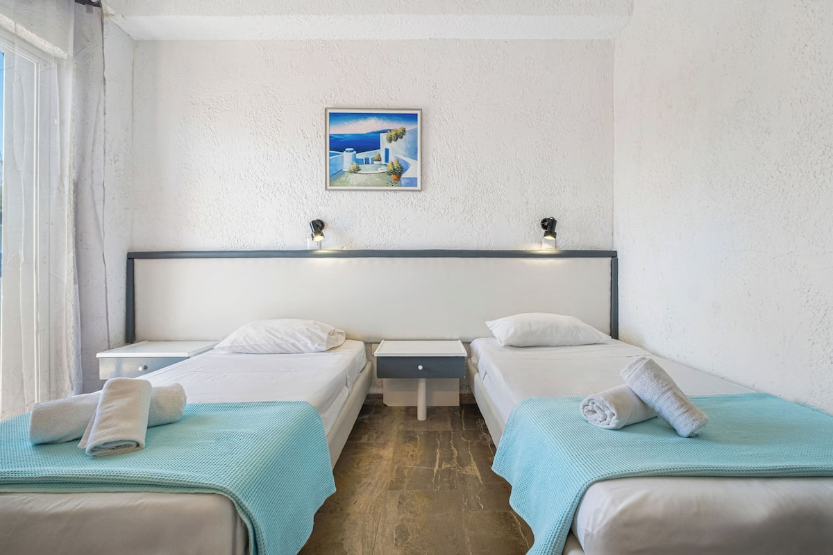 A hotel room with two beds, a nightstand, a painting on the wall, and a window.