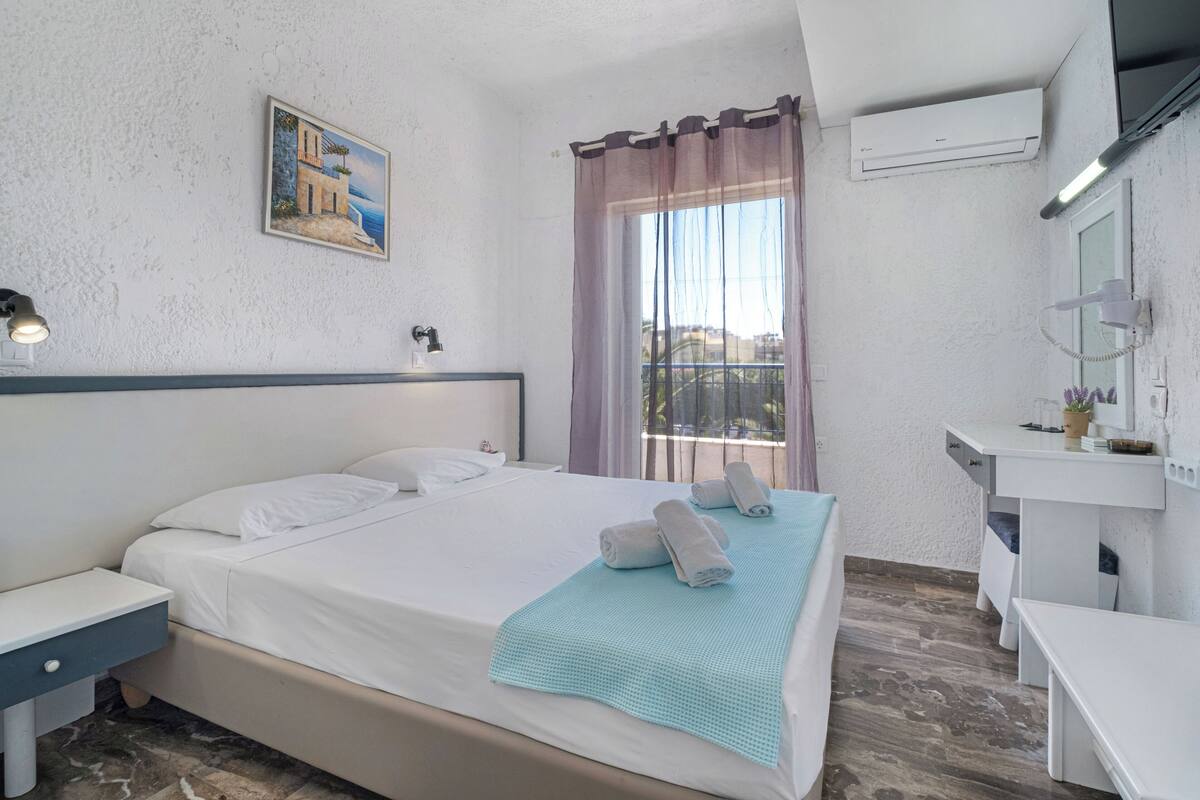 A hotel room with a bed, bedside table, and a desk with a chair.