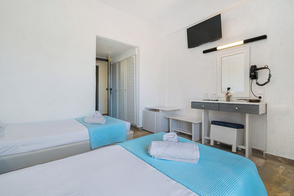 A hotel room with two beds, a desk, a chair, a TV mounted on the wall, and a bathroom door.