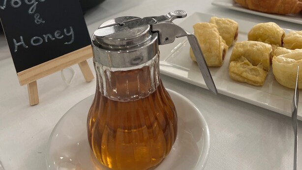 A breakfast buffet with a sign for yogurt and honey, a honey dispenser, and pastries. - Gorgona Hotel (Malevizi)
