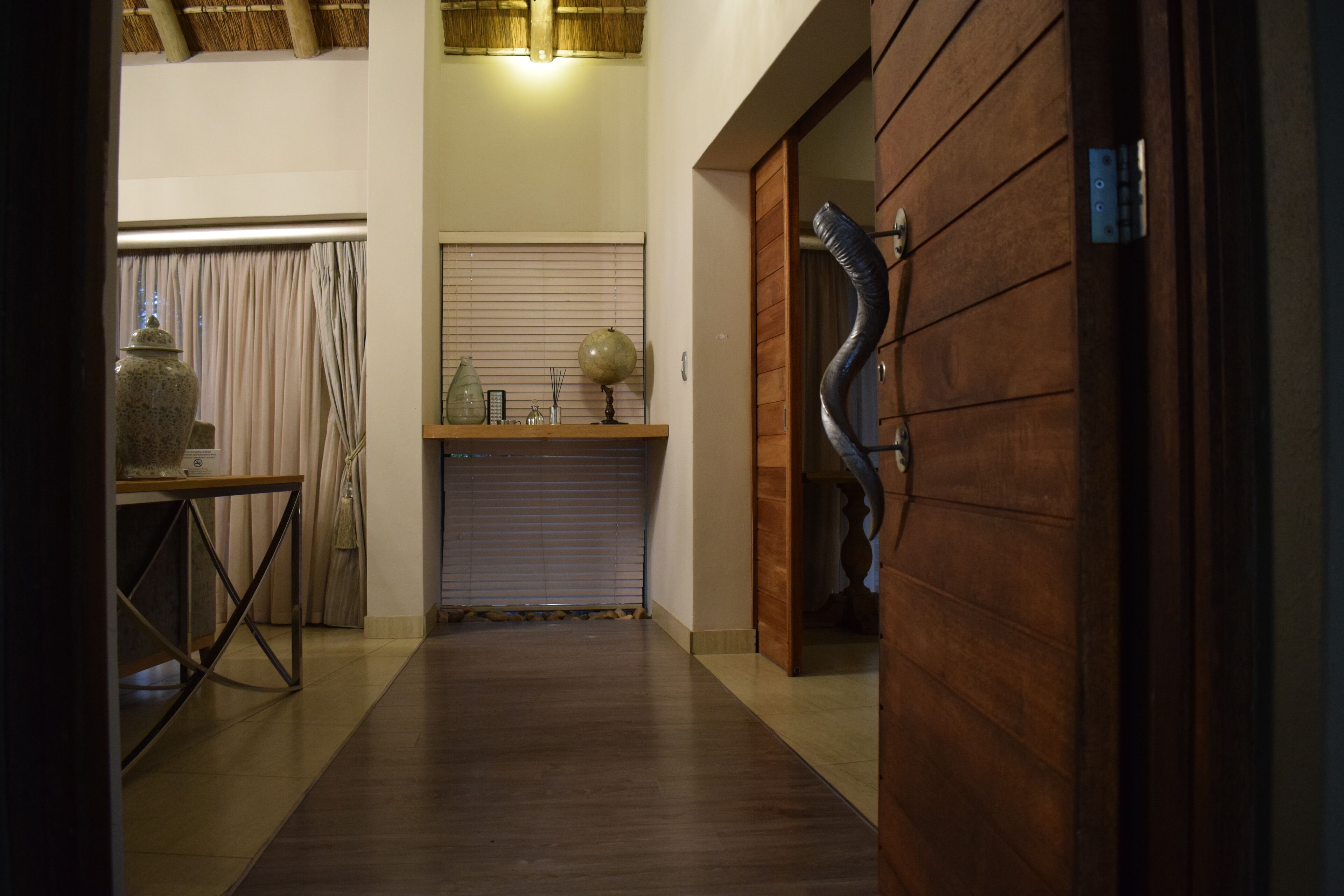 A hallway with a wooden floor, a table with a vase, a globe, and a shutter door.