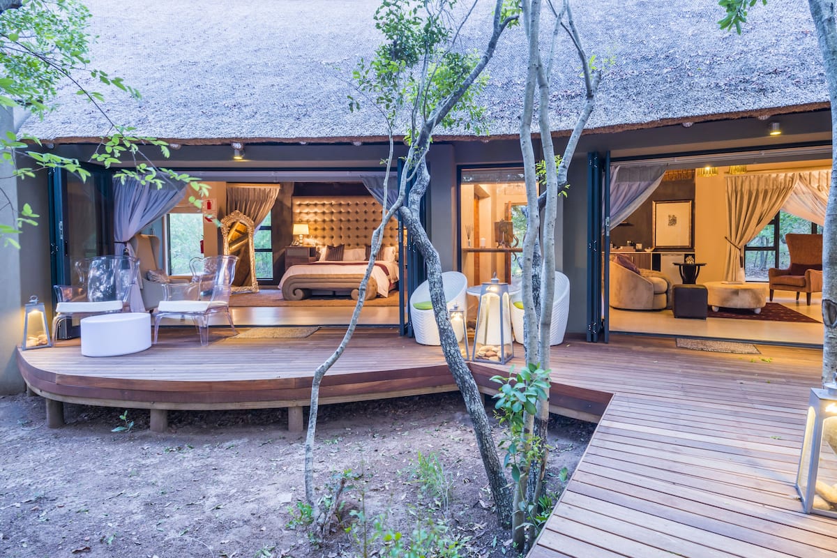 A modern outdoor living area with a wooden deck, seating, and a thatched roof structure.