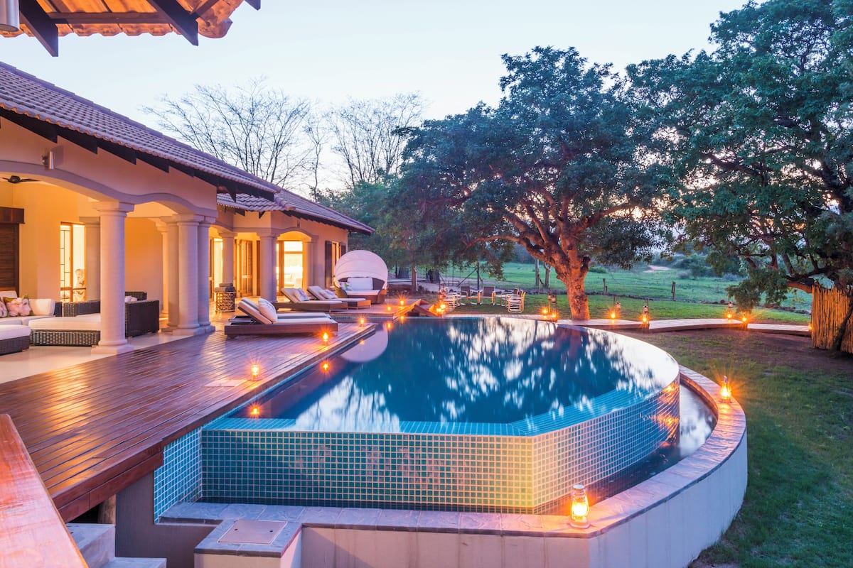 A swimming pool with a tiled deck, lounge chairs, and a covered seating area.