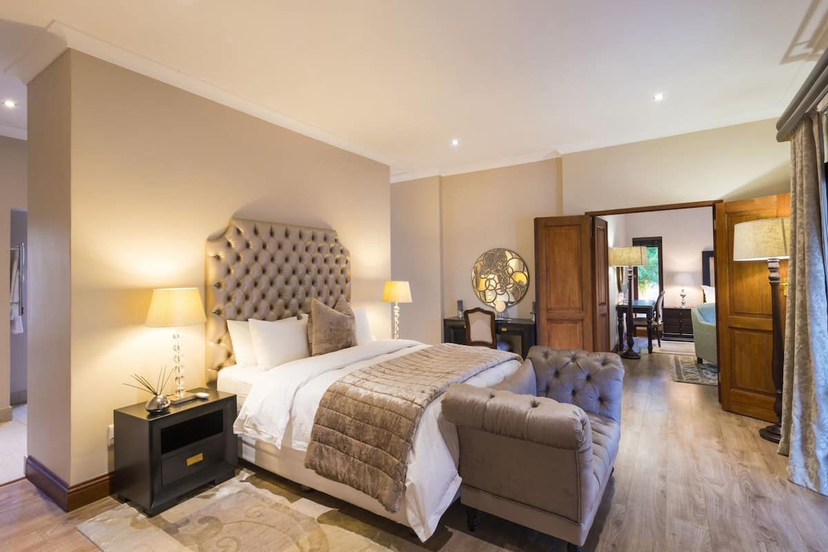 A bedroom with a large bed, bedside tables, a nightstand, a chair, a wooden door, and a mirror.