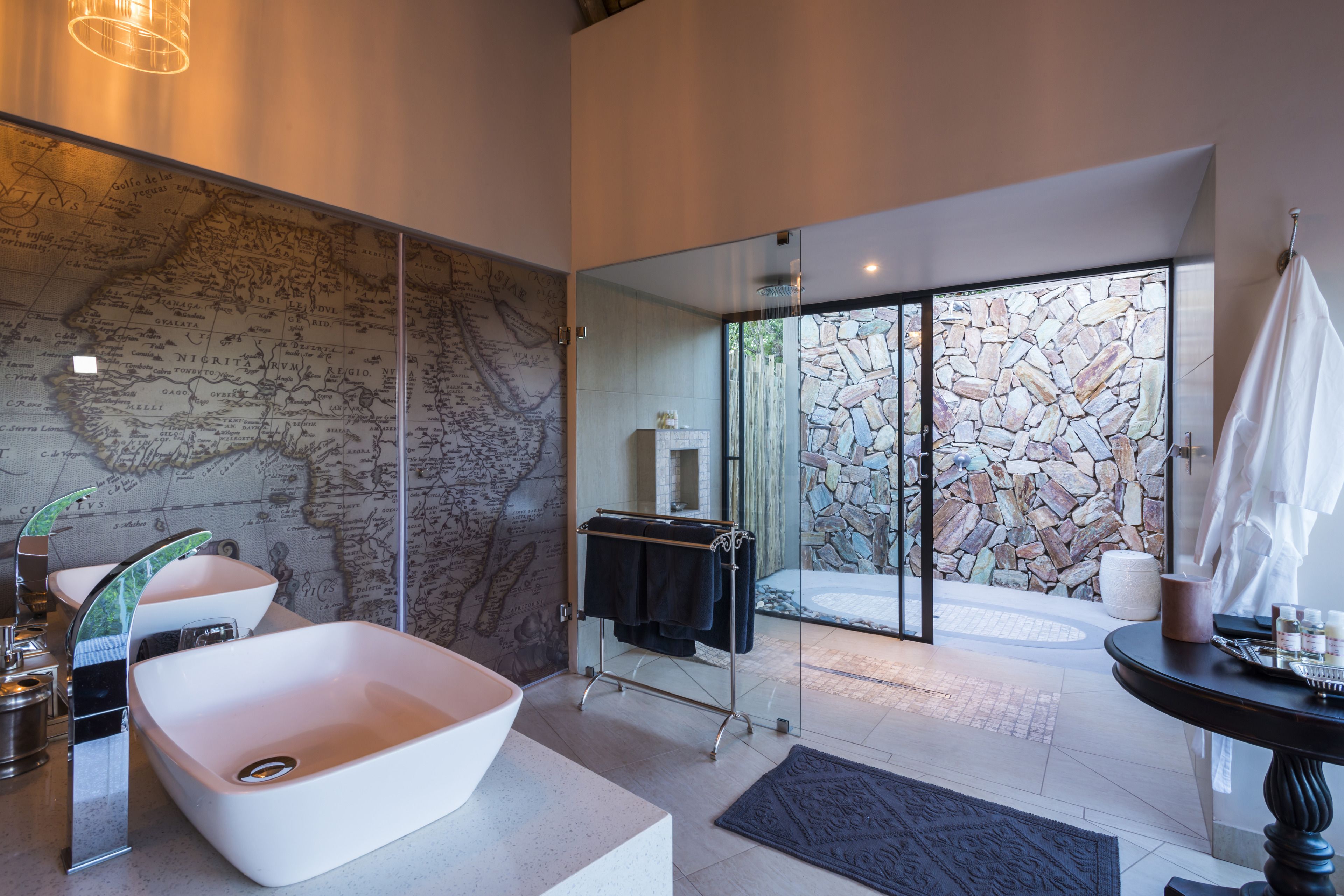 A modern bathroom with a large sink, a map wall, and a stone wall leading to a balcony.
