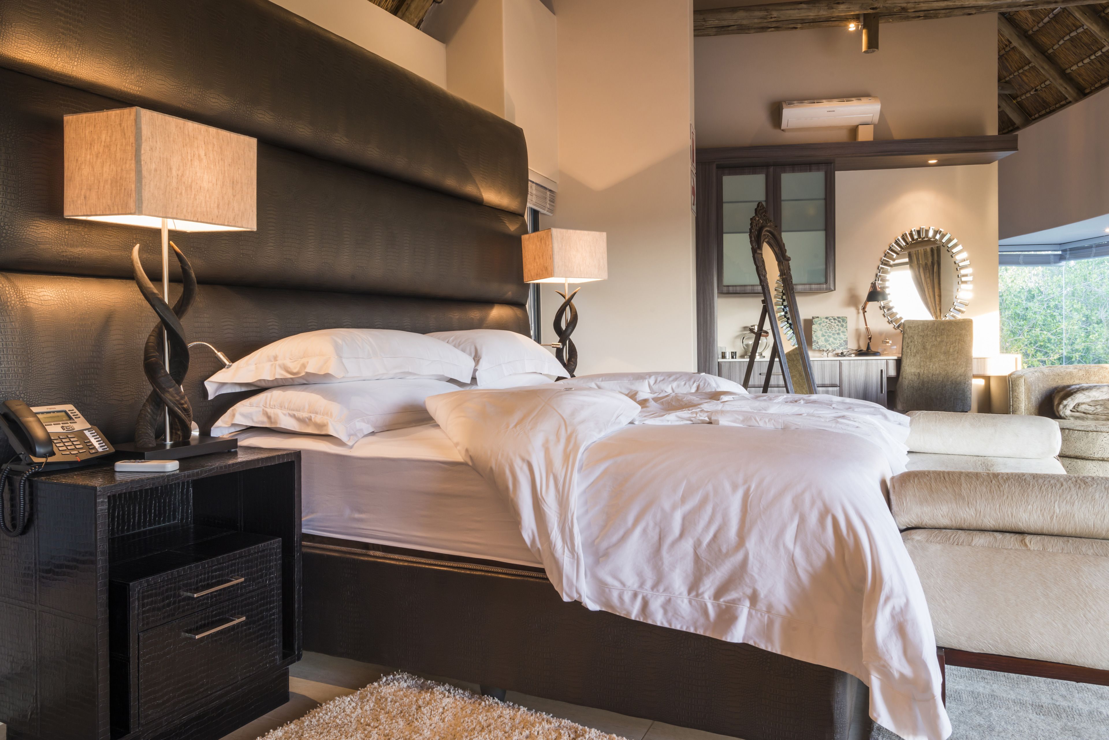 Un dormitorio con una cama grande, lámparas de noche, una mesita de noche con un teléfono y un espejo.