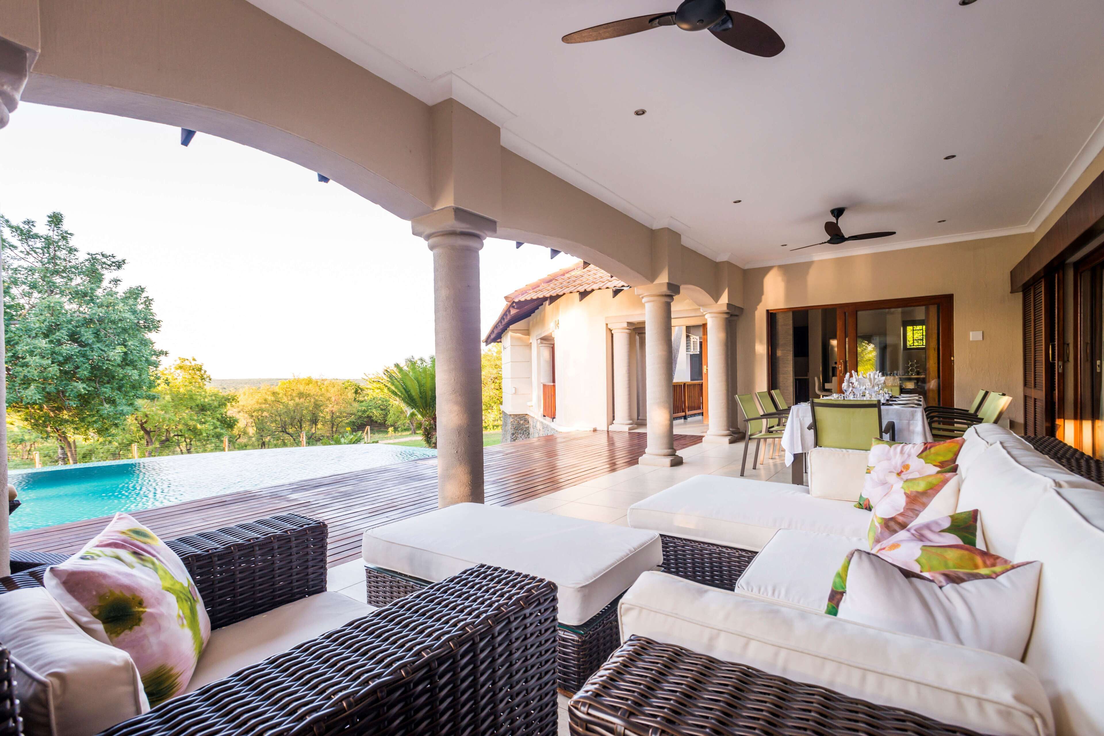 A covered outdoor seating area with wicker furniture, a pool, and a view of the landscape.