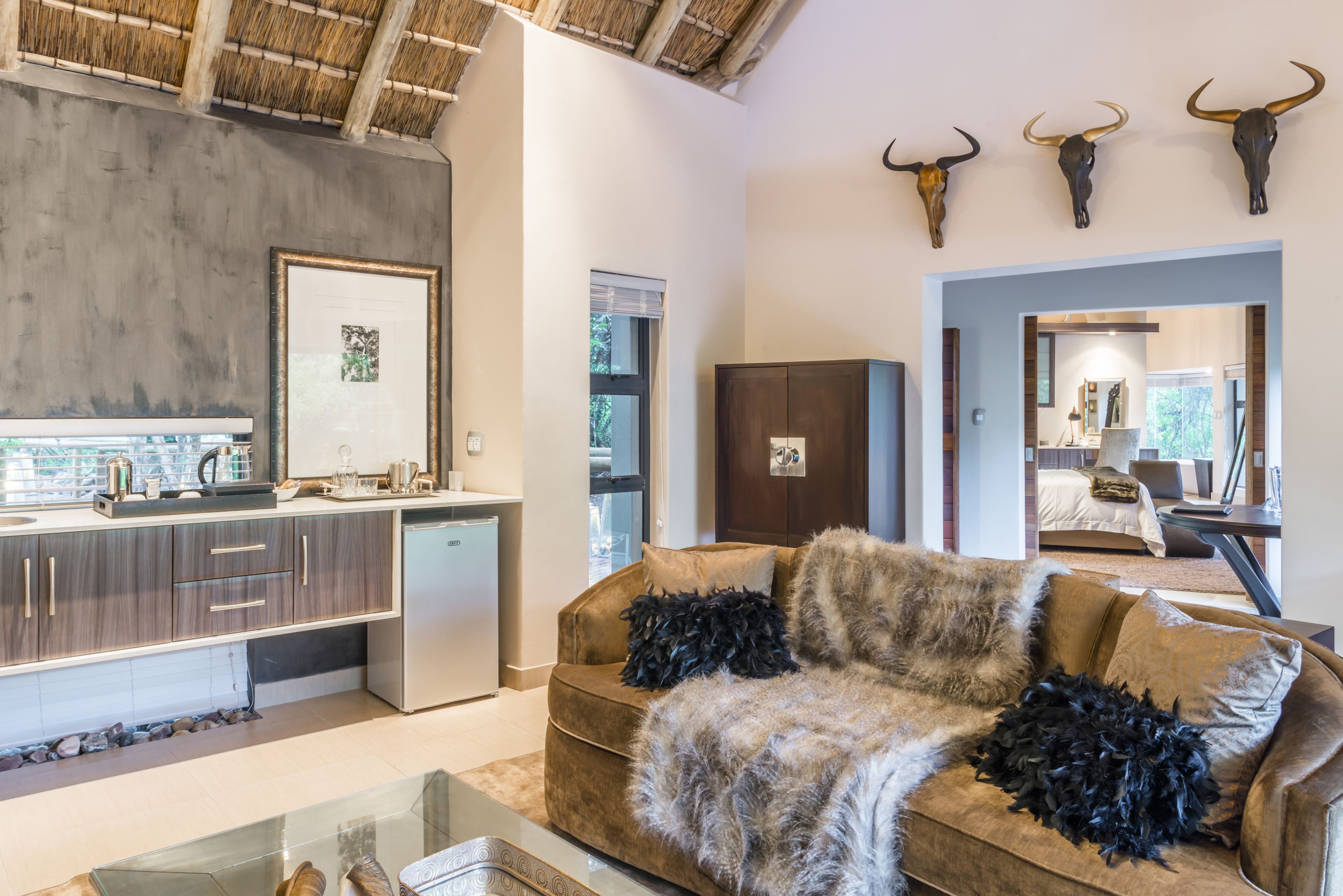 Una sala de estar moderna con un sofá, una mesa de centro de vidrio y una cocina con un lavamanos y armarios.