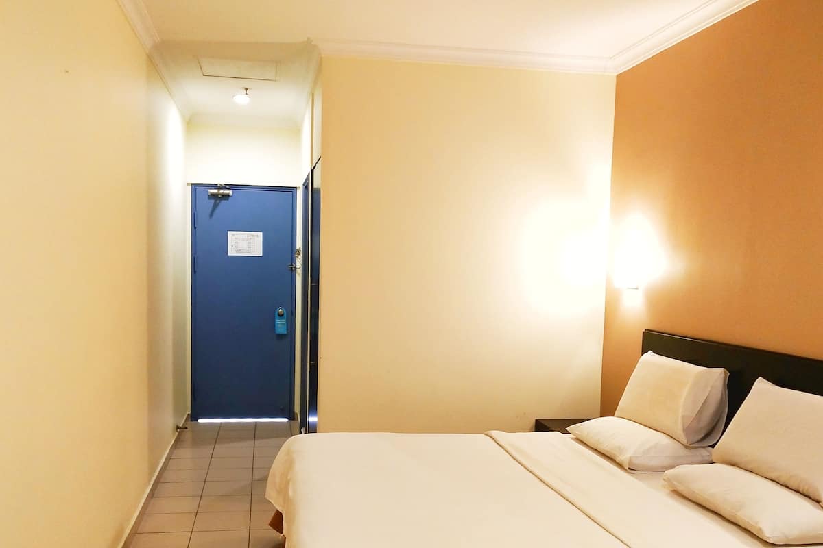 A hotel room with a bed, a nightstand, a wall-mounted lamp, and a door leading to another room.