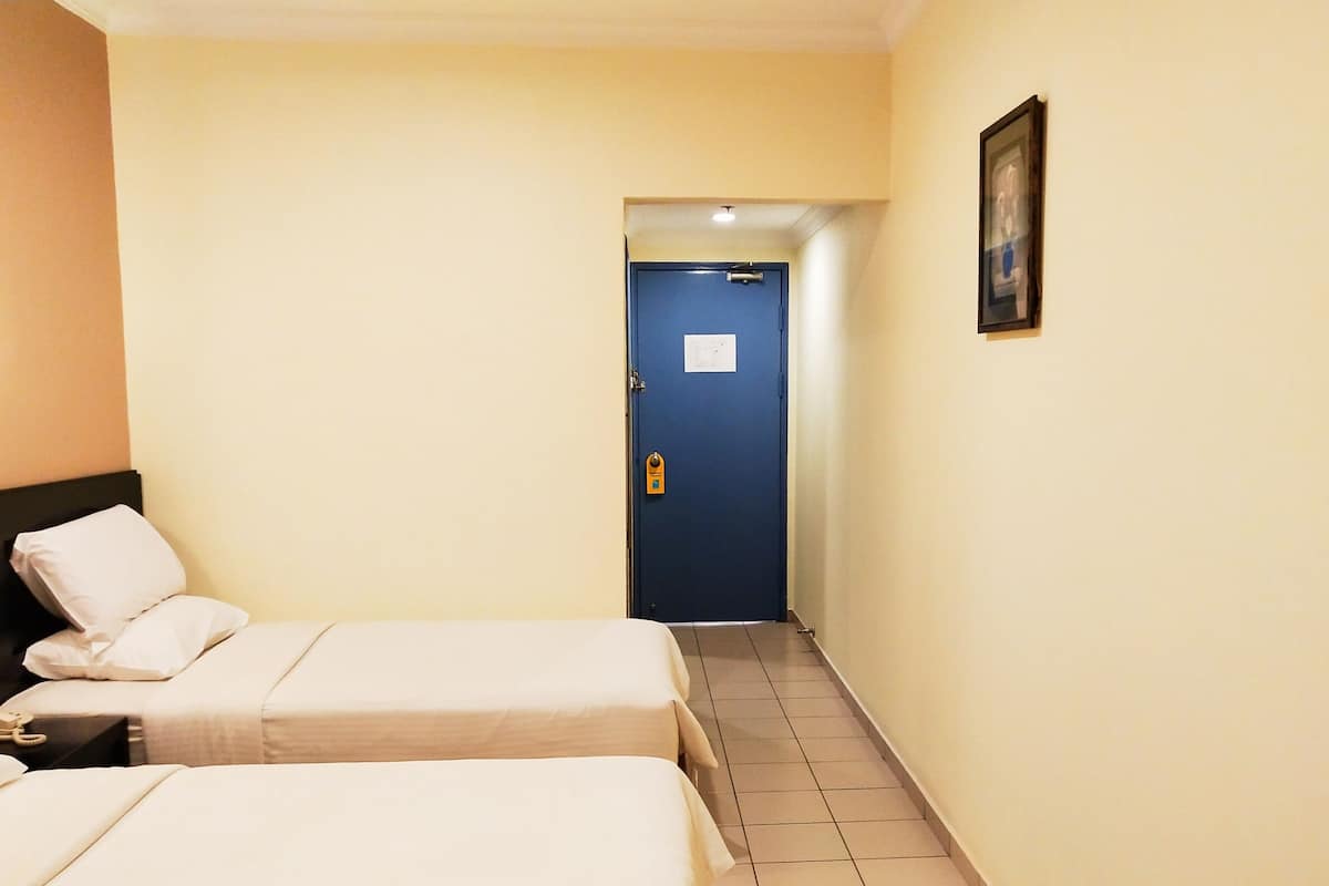 A hotel room with two single beds, a nightstand with a telephone, a blue door, and a framed picture on the wall.