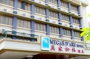 En hotellbyggnad med en skylt som visar texten "MEGAH D'ARU HOTELS" och "美家松林酒店", vilket är hotellets namn på kinesiska.