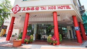 A hotel entrance with red pillars, a sign in Chinese and English, and potted plants. - Tai Hoe Hotel (Singapore)