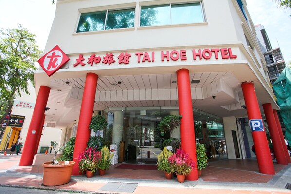 A hotel entrance with red pillars, a sign in Chinese and English, and potted plants. - Tai Hoe Hotel (Singapore)