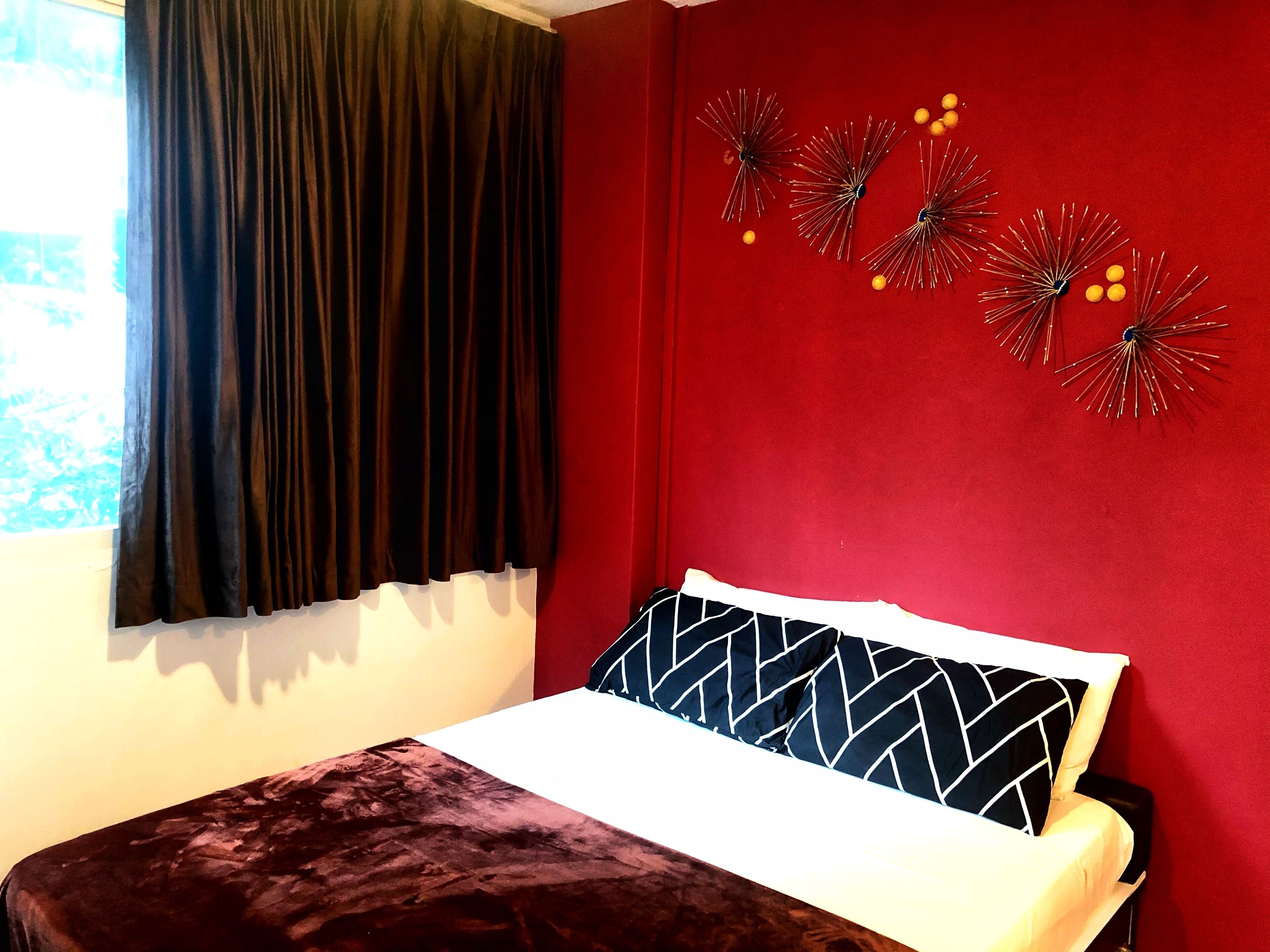 Un dormitorio con cama, cortinas oscuras, pared roja y decoración en la pared.