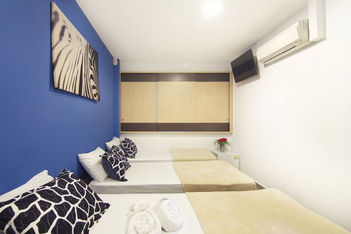 A hotel room with a blue accent wall, a bed with patterned pillows, a bedside table with a vase of flowers, and a mounted TV.