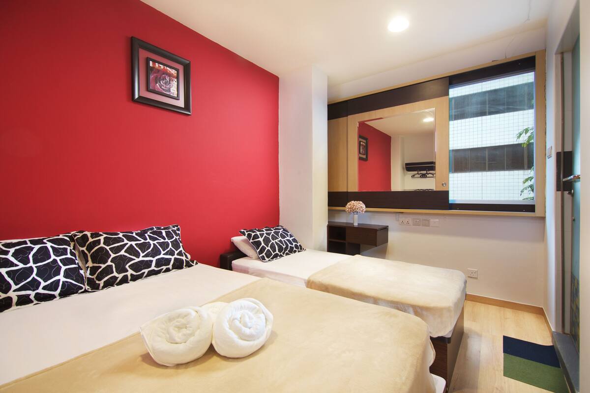 A hotel room with two beds, red walls, a large mirror, and a view of a building outside.