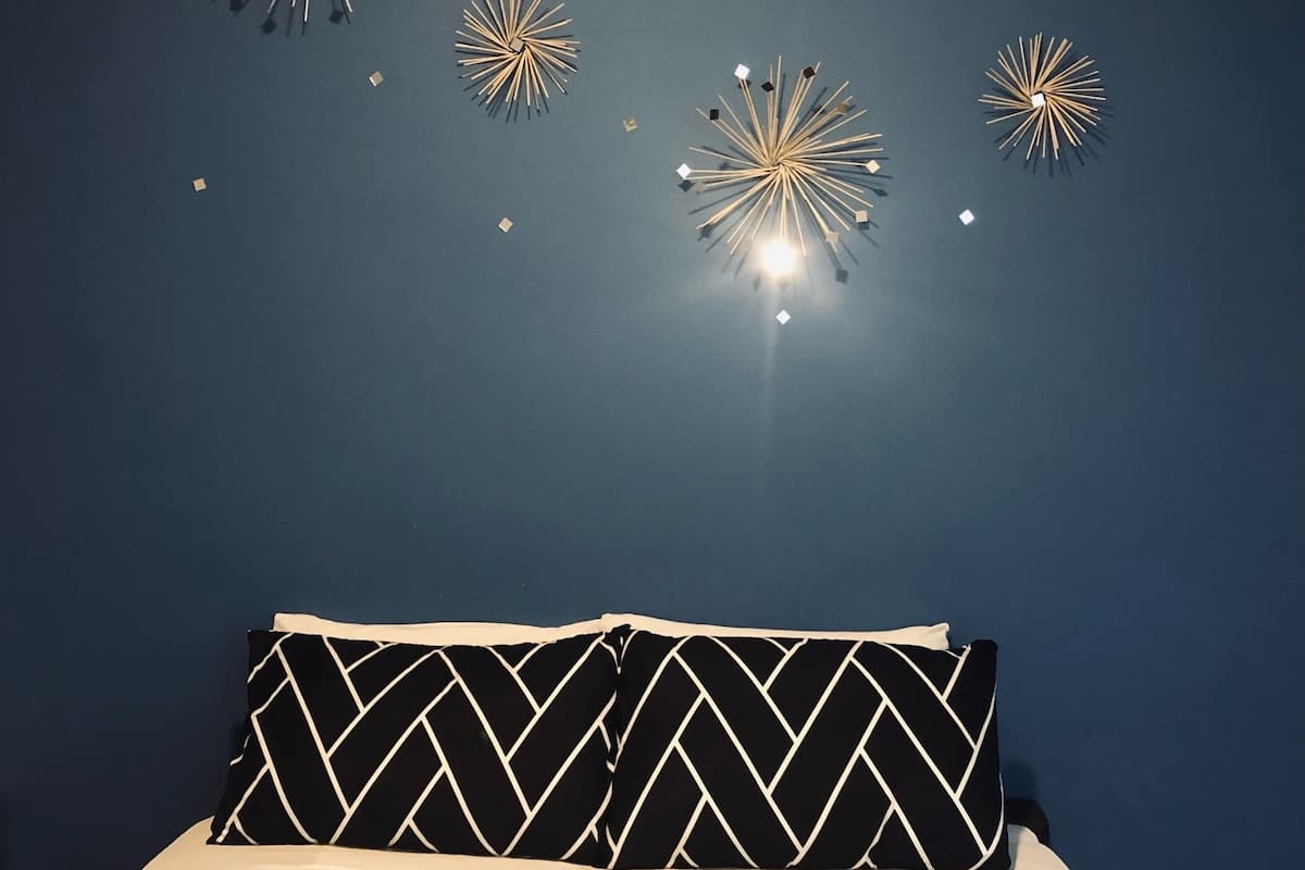 A bed with a brown headboard, a white sheet, and two black and white patterned pillows.