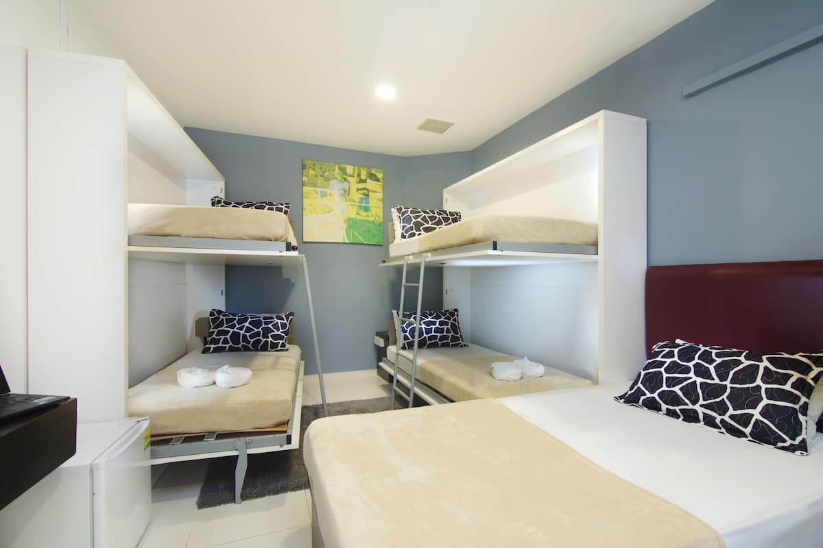 A dormitory room with bunk beds, a desk, and a painting on the wall.