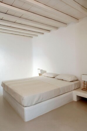A minimalist bedroom with a large bed, white walls, and a simple wooden ceiling. - Elia White Residence (Mykonos)