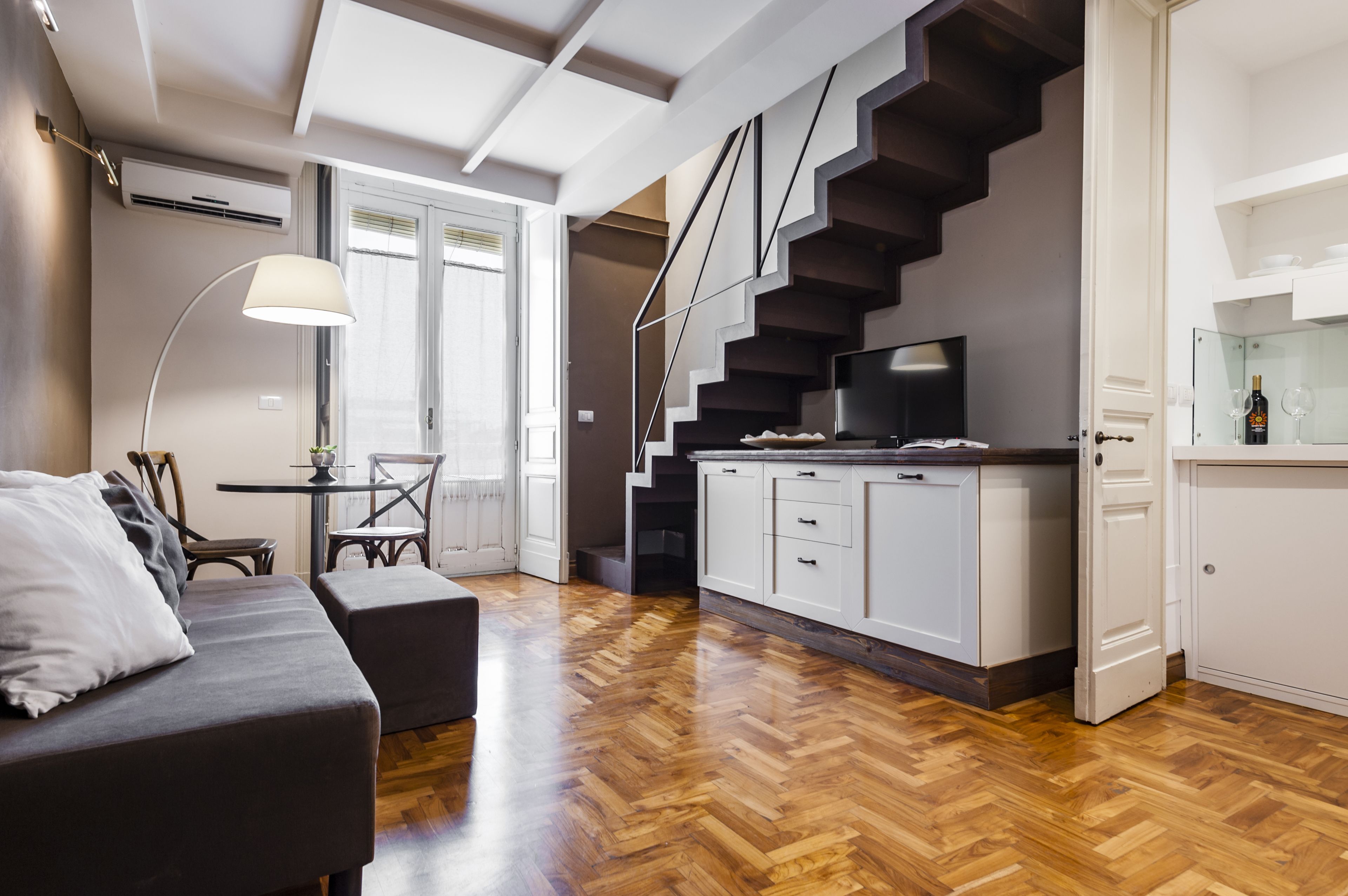 A modern living space with a sofa, dining table, and a staircase leading to a kitchen area.