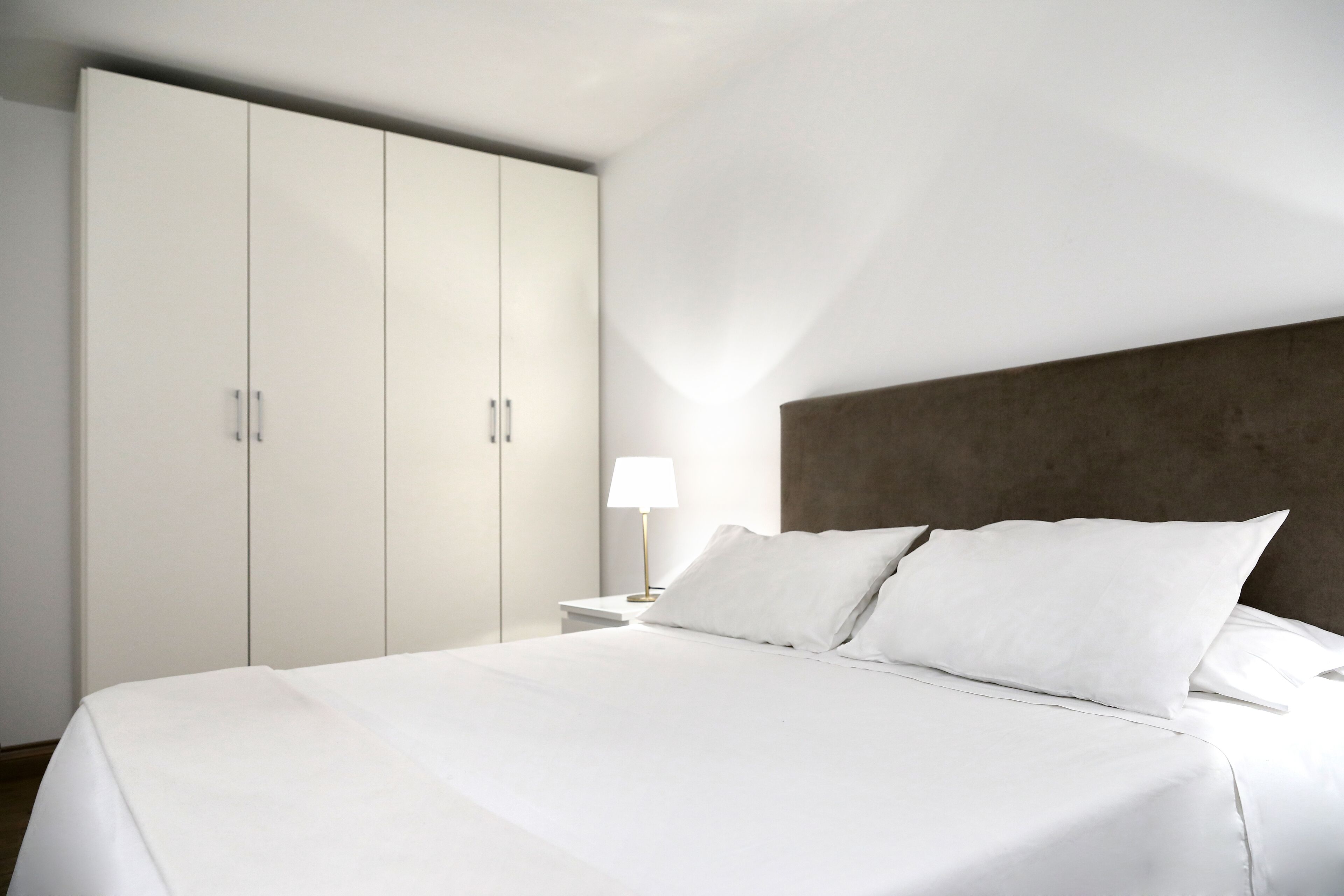 A modern hotel room with a large bed, a nightstand, a lamp, and a wardrobe.