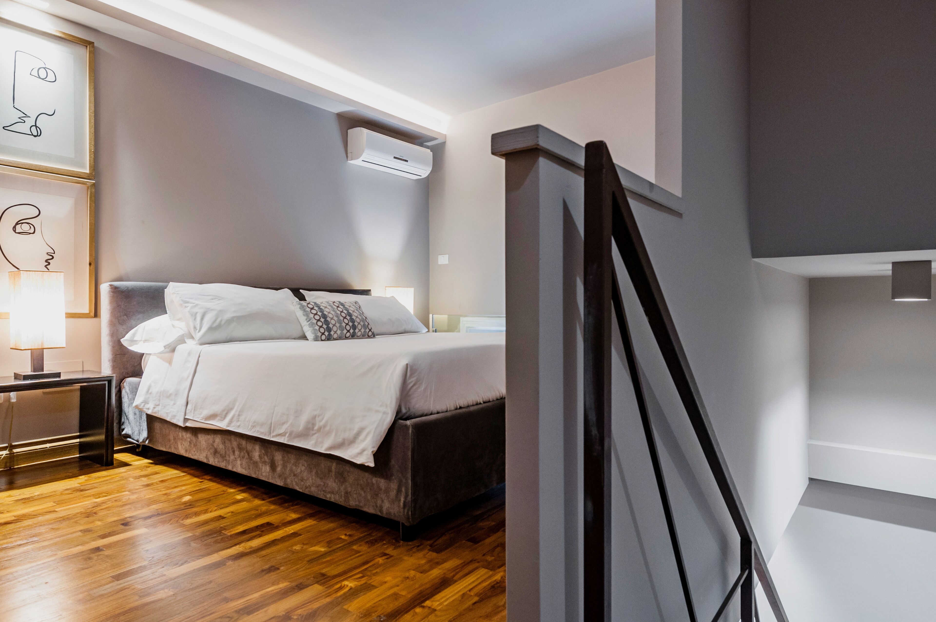 Ein modernes Schlafzimmer mit Holzboden, einem Bett mit weißer Bettwäsche, einem Nachttisch mit Lampe und einer wandmontierten Klimaanlage.