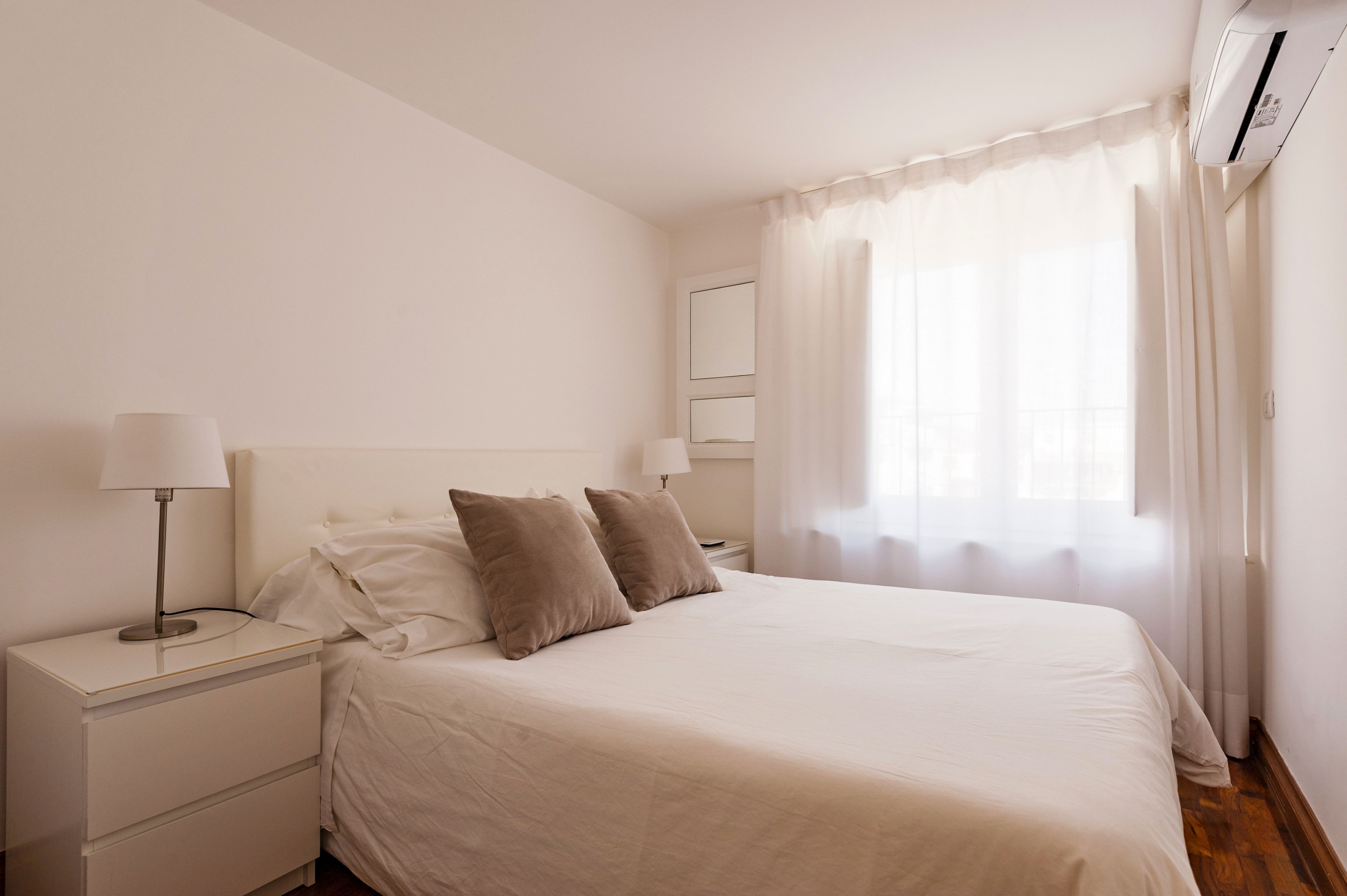 A bedroom with a bed, two bedside tables, a lamp, and a window with curtains.