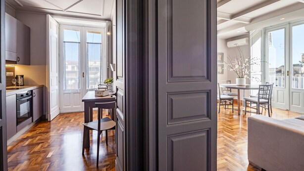 A modern kitchen with a dining area, wooden flooring, and large windows.