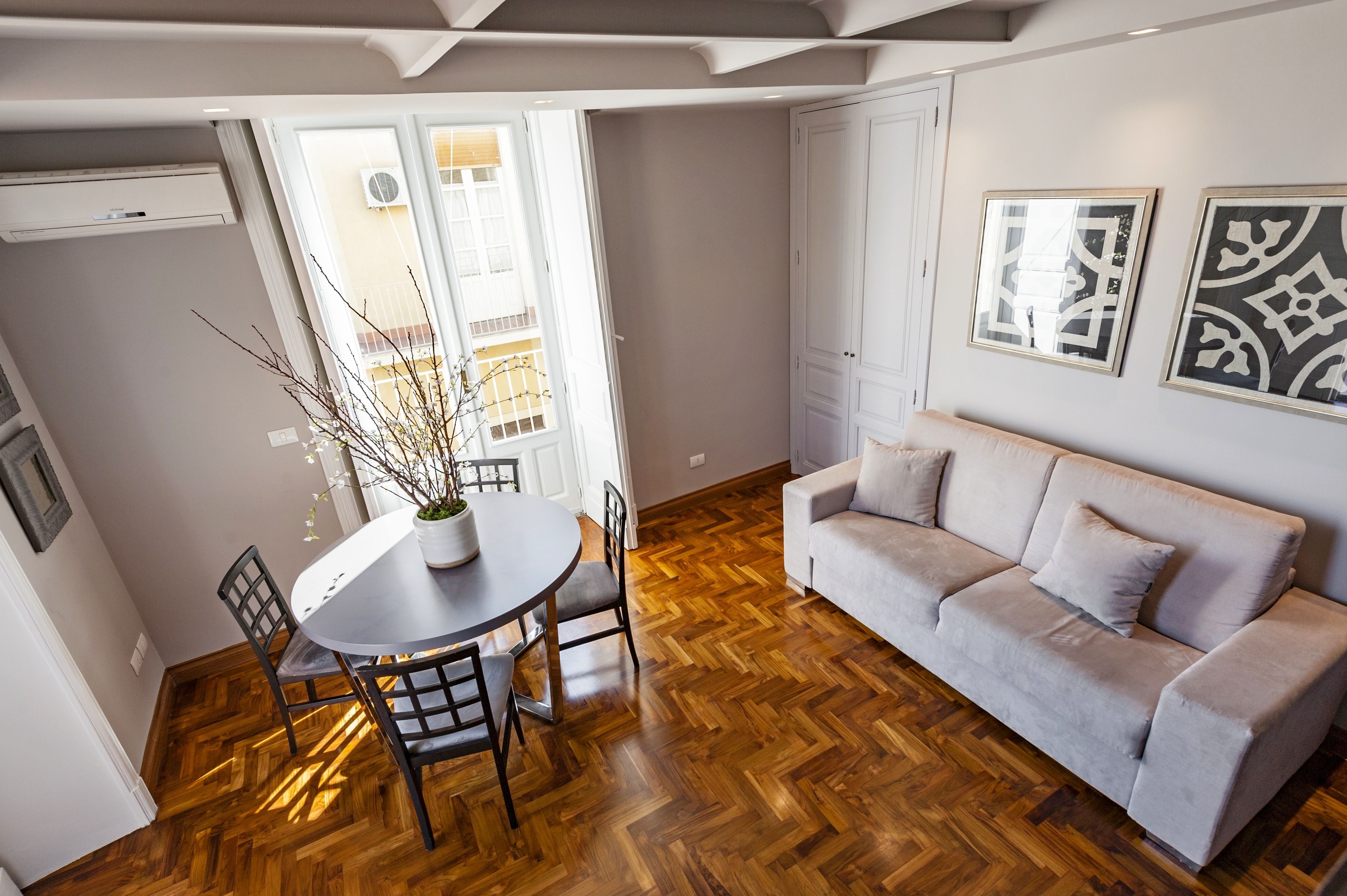 Une pièce dotée d’un parquet en bois disposé en motif à chevrons, d’une table de salle à manger ronde avec des chaises, d’un canapé et de deux œuvres d’art encadrées accrochées au mur.