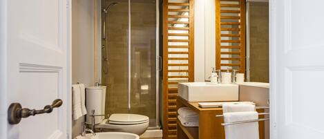 Une salle de bain équipée d’une douche, de toilettes, d’un bidet et d’un meuble-lavabo en bois avec un miroir.