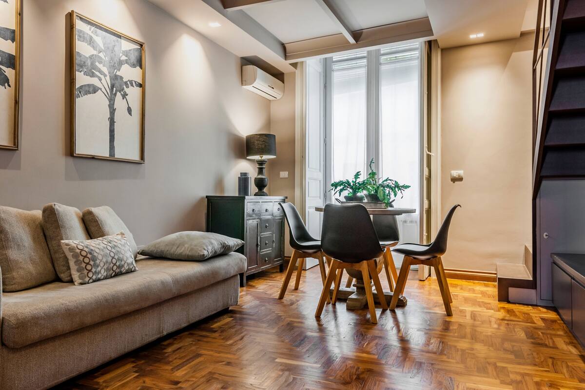 A modern living room with a sofa, dining table, chairs, and a potted plant.