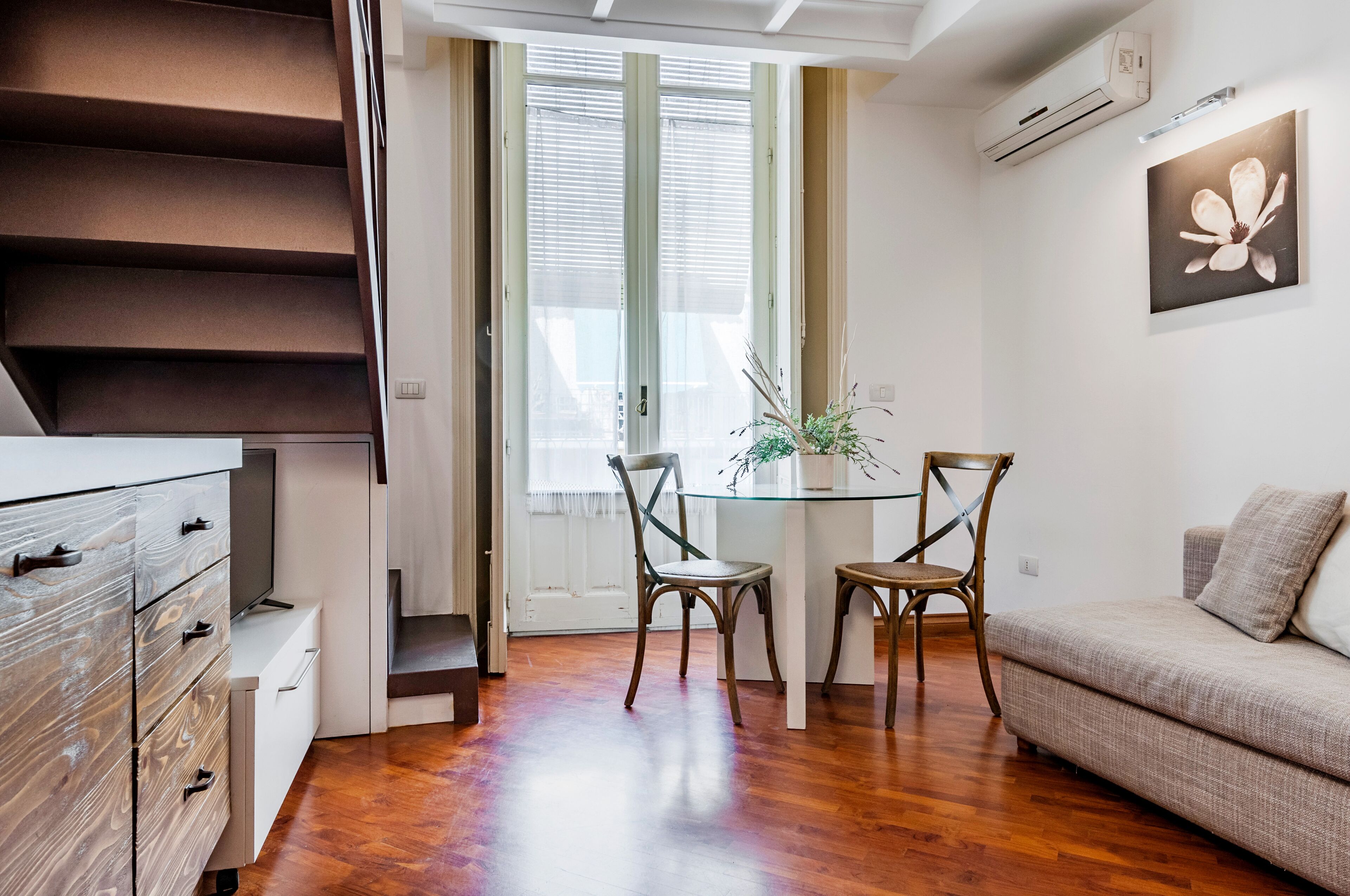 Un salon moderne avec un escalier, un coin repas comprenant deux chaises et une table, et un canapé.