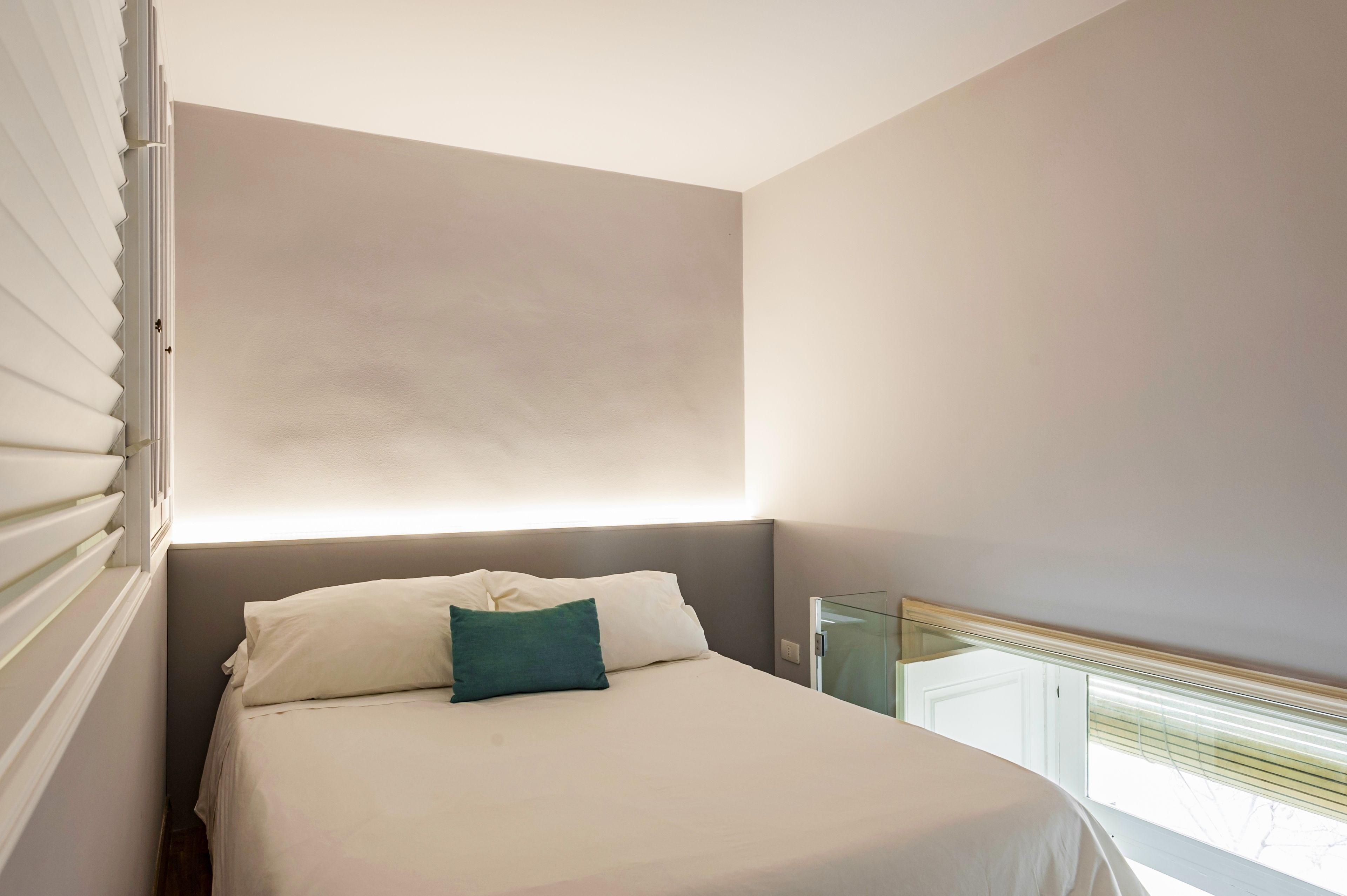 A bedroom with a bed, a nightstand, and a window with blinds.