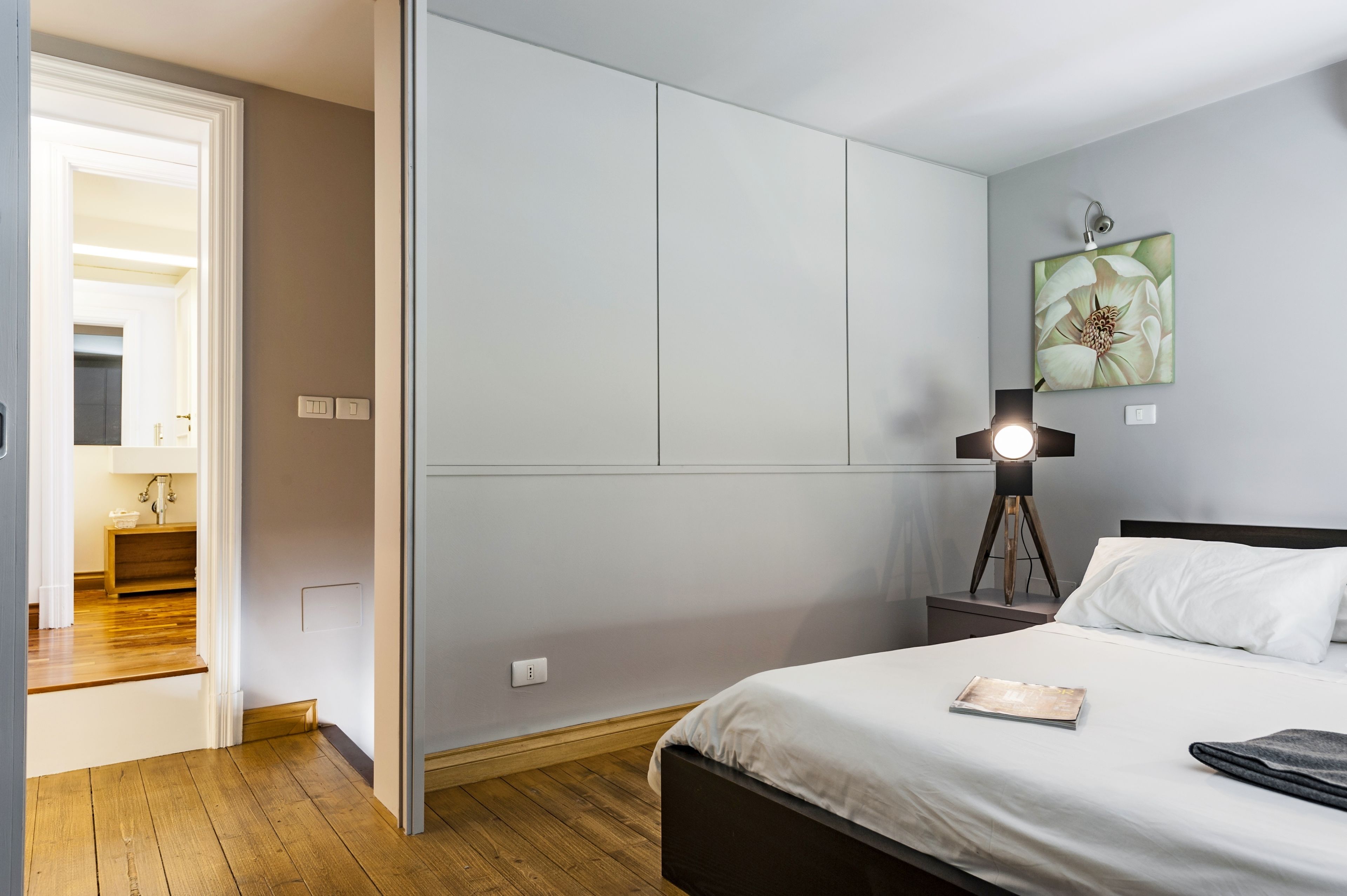 A bedroom with a bed, bedside table, lamp, and a painting on the wall.