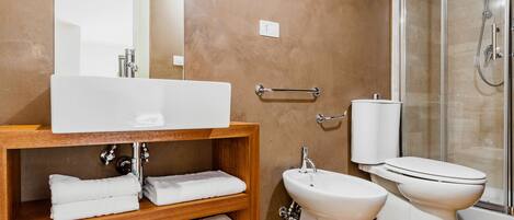A bathroom with a wooden vanity, a large mirror, a white sink, a bidet, a toilet, and a glass shower enclosure.