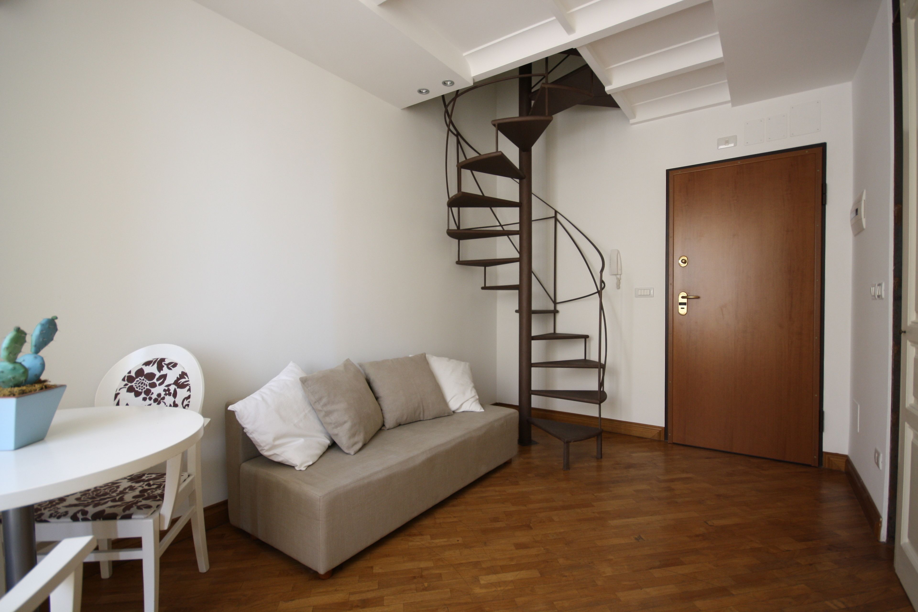 Una sala de estar moderna con una escalera espiral, un sofá, una mesa de comedor y piso de madera.