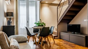 A modern living room with a sofa, a dining table with chairs, a TV, and a staircase.