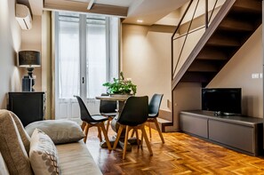 A modern living room with a sofa, dining table, chairs, a TV, and a staircase. - Ferrini Home Residence 150 (Catania)