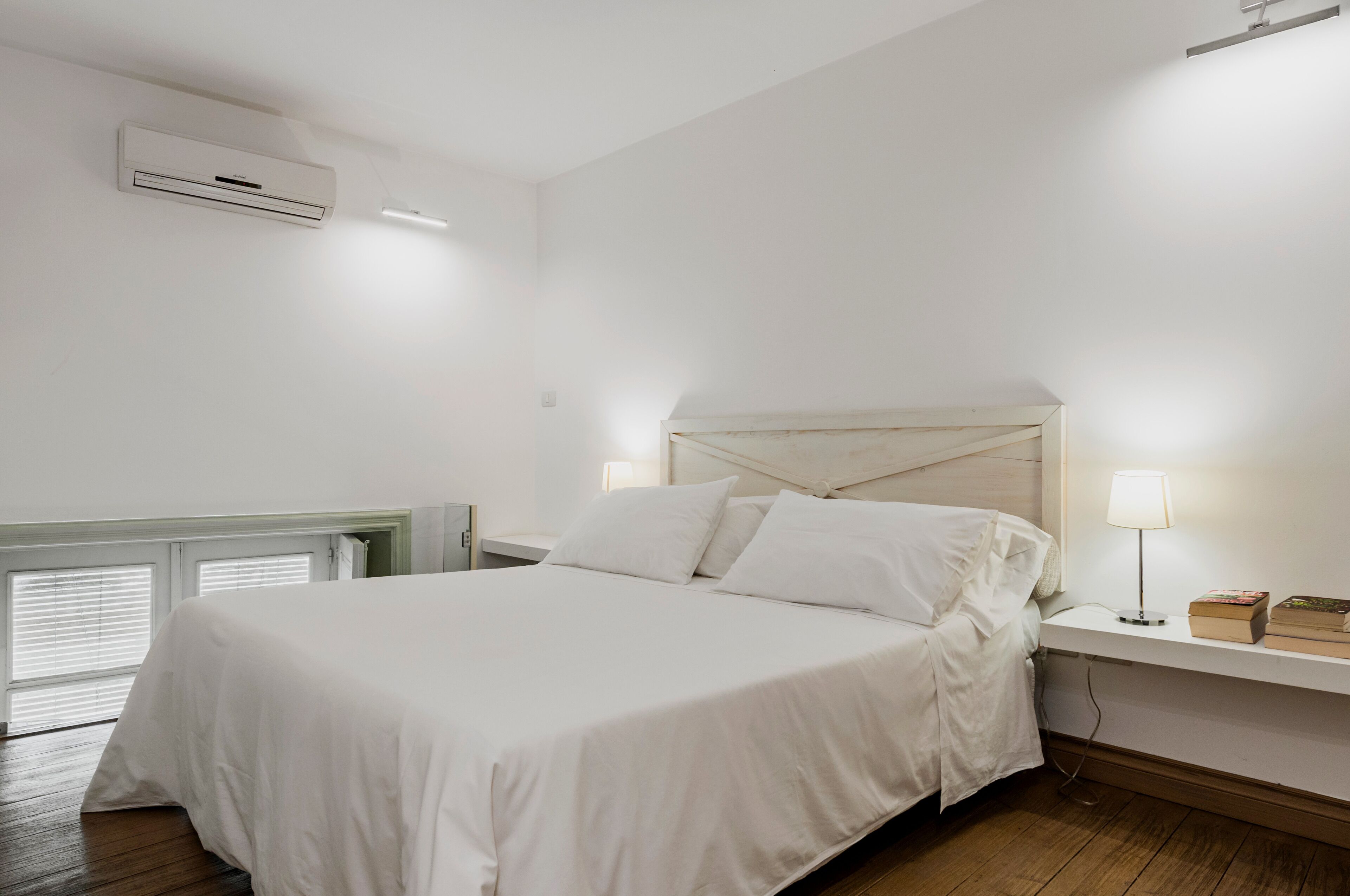 A bedroom with a bed, bedside tables, a nightstand, a lamp, and an air conditioning unit.