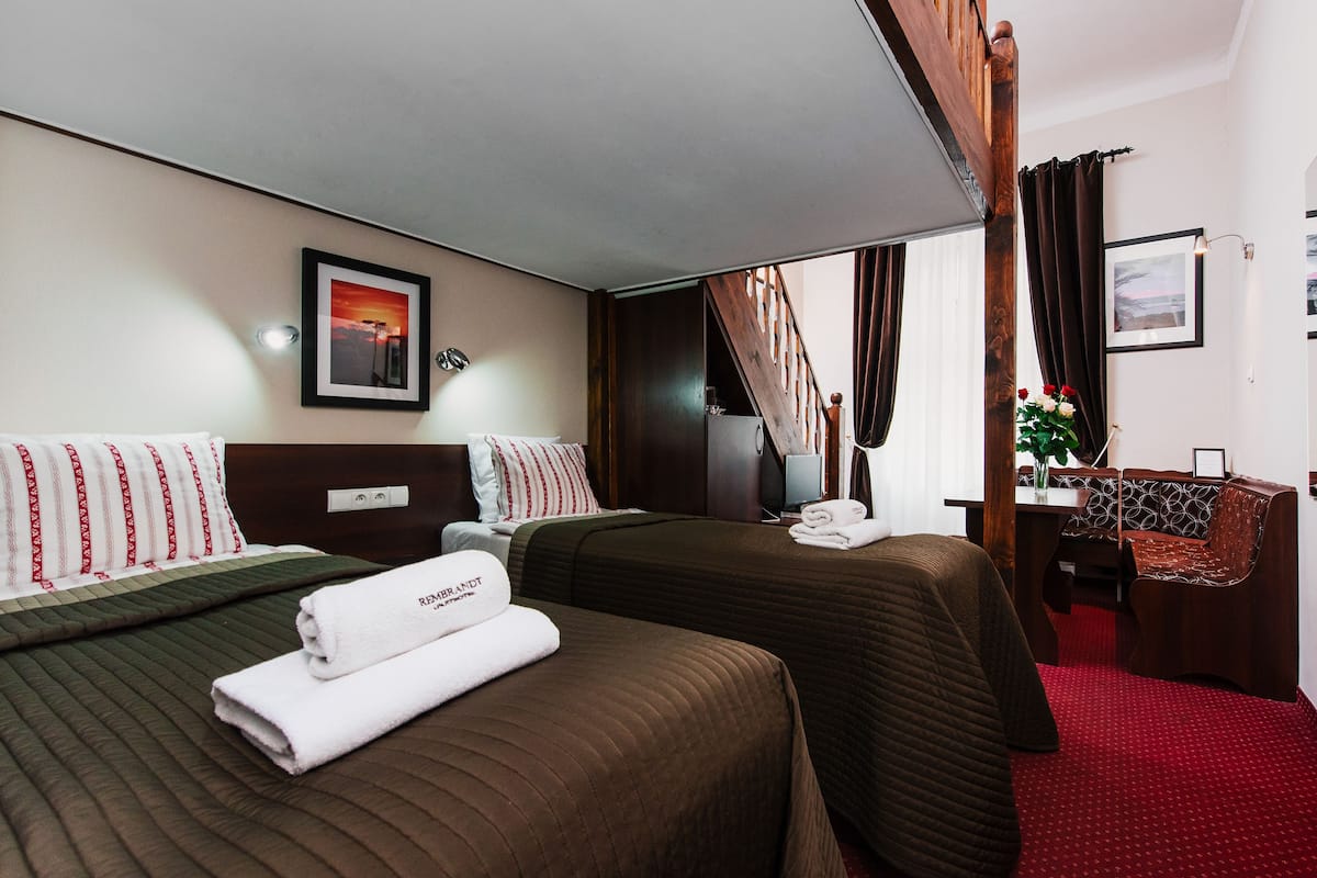 A hotel room with two beds, a desk, a chair, and a view of the sunset.