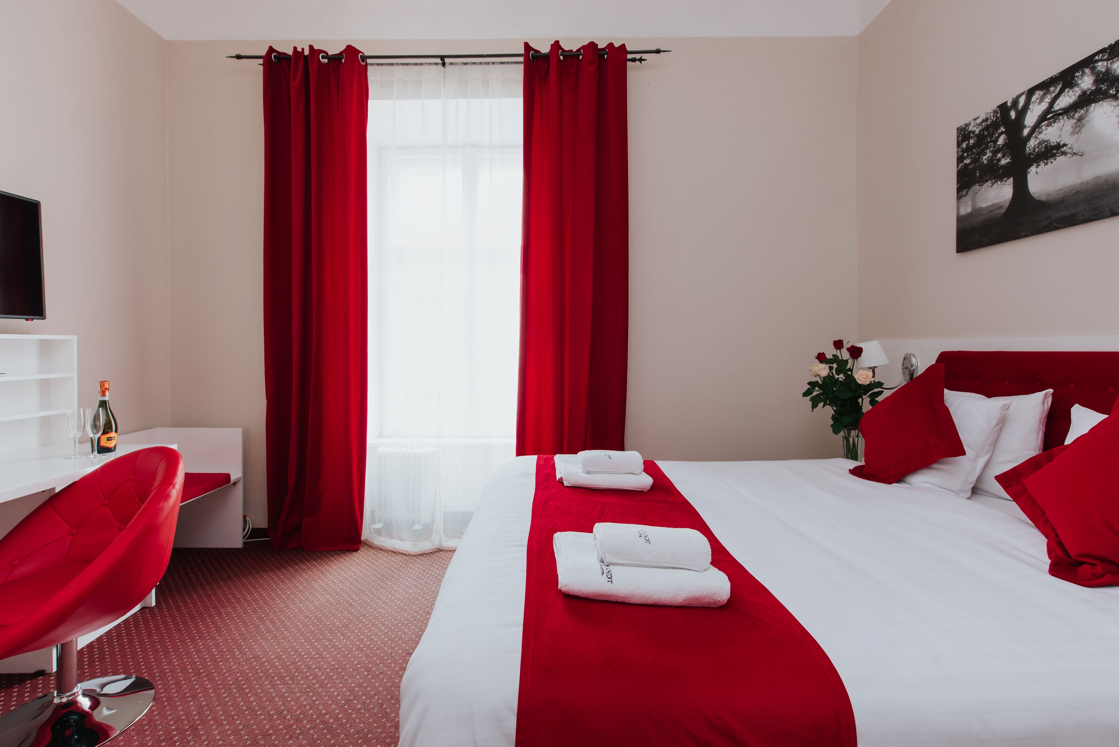 A hotel room with a bed, red curtains, a TV, a desk, and a chair.